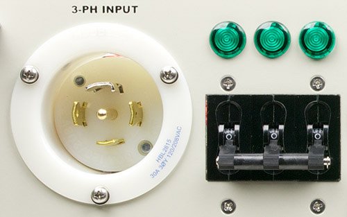 A closeup photo of a recessed three-phase, twist-lock power inlet connector next to a main breaker and indicators.